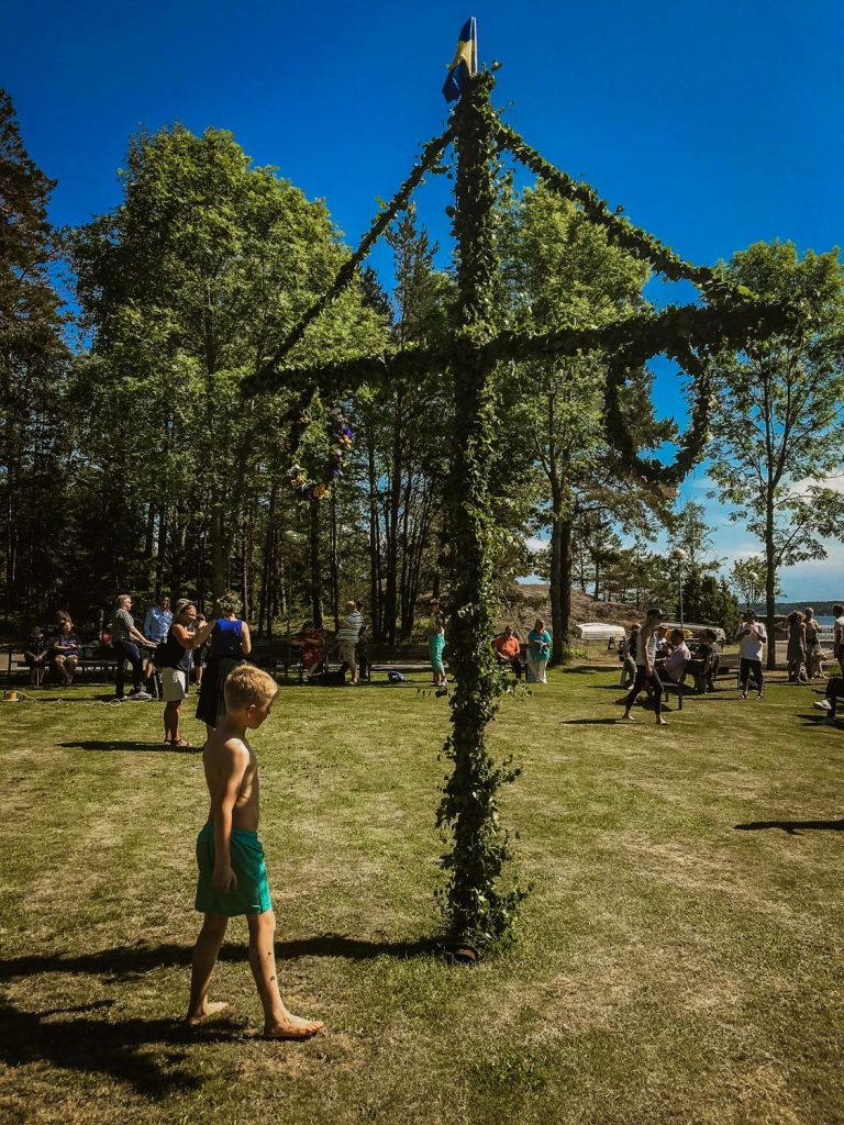 Dans runt midsommarstången. Himlen är blå.