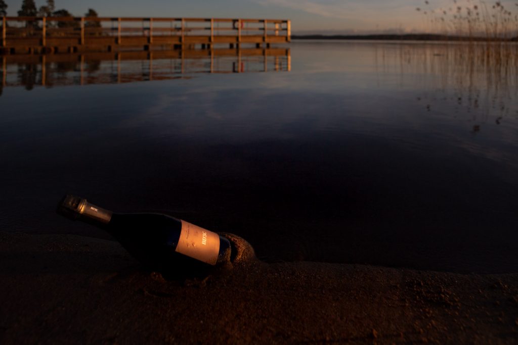 Champagneflaska på stranden en sensommarkväll. Almåsas brygga i bakgrunden.