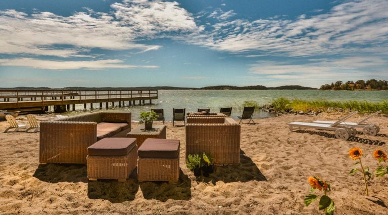 Sommar på stranden, sommarmöbler står vid havskanten, solen skiner och himlen är blå med vita moln.